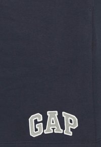 Dark navy fabric with white embroidered letters "GAP" in block style on the lower edge of the garment.