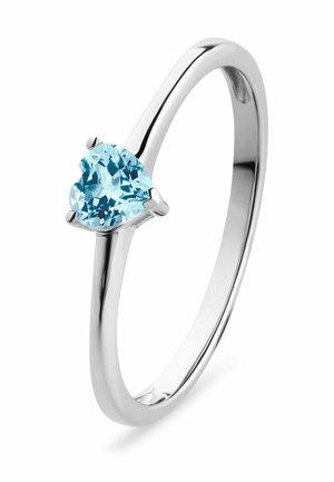 Zilveren ring met een gepolijste band, voorzien van een hartvormige lichtblauwe edelsteen die is gezet in drie klauwen. Gladde, reflecterende afwerking.