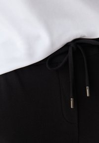 Svarta joggerbyxor med dragsko i midjan i svart. Dragskon har metallspetsar. En vit t-shirt syns delvis ovanför.