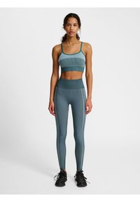 Conjunto de activewear en color verde azulado que incluye un sujetador de canalé y leggins de cintura alta con rayas laterales. Combinado con zapatillas deportivas negras. Textura suave.