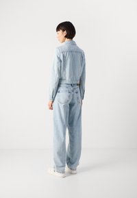 Lys blå denim cropped jakke og løse jeans, med klassisk krage, knappelukking og fem-lommers design. Hvite sneakers.