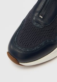 Μπλε ναυτικό αθλητικό παπούτσι με  επάνω μέρος από δίχτυ, λεπτομέρειες από δέρμα, υφή και καφέ λαστιχένια σόλα. Κοντινό πλάνο που δείχνει τις ραφές και τα φερμουάρ.