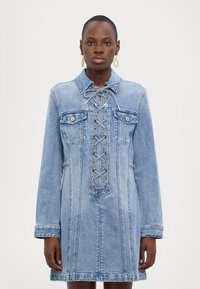 Denimkjole i lyseblå med lange ermer, snøring foran med metalløyer, to brystlommer og en avslappet passform.