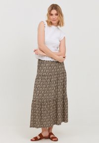 Biela top bez rukávov s volánmi, skombinovaná s vzorovanou, vrstvenou maxi sukňou v hnedej a béžovej farbe. Hnedé sandále na slidovanie dotvárajú celý outfit.