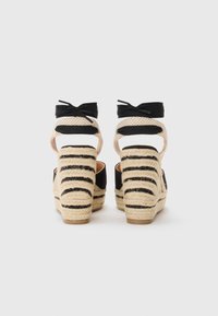 Sandales compensées en espadrille noires et beiges avec des talons en jute rayés, dos ouvert et accents en ruban sur les brides de cheville.