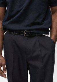 Marinefarbener Strickshirt kombiniert mit dunklen, gef alteten Hosen. Schwarzer Ledergürtel mit einer silbernen Schnalle. Nahaufnahme des Bereichs um die Taille und der oberen Oberschenkel.