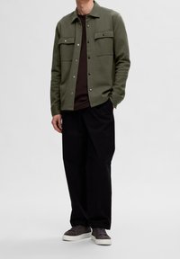 Oliivinvihreä napillinen takki, jossa kaksi rintataskua, päällä tummanruskea paita. Yhdistetty löysiin mustiin housuihin ja harmaisiin lenkkareihin.