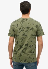 Camiseta de algodón verde con un patrón de hojas de bambú negras, de mangas cortas y diseño de cuello redondo clásico.