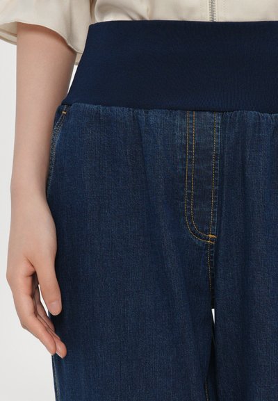 Denim pants with a navy elastic waistband. Features a relaxed fit with visible yellow stitching and pockets. No additional embellishments.