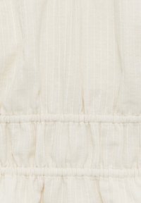 Gros plan sur un tissu crème froissé avec de fines rayures blanches verticales et des coutures élastiques horizontales froncées.