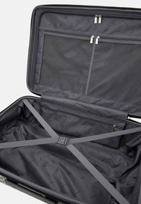 Black suitcase interior with zippered mesh pocket, elastic straps, and logo-patterned fabric lining, featuring a smooth texture and structured shape.