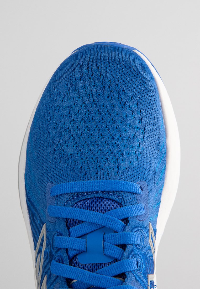 Blauer Sportschuh mit einem strukturierten Strickobermaterial, ausgestattet mit einer weißen Sohle und blauen Schnürsenkeln. Das Design ist leicht und hat eine abgerundete Spitze.