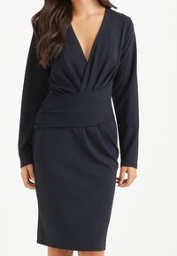 Navyblaues Kleid mit tiefem V-Ausschnitt, langen Ärmeln und tailliertem Schnitt. Verfügt über Drapierungen und einen Bleistiftrock, gefertigt aus einem glatten Stoff.