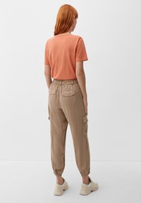 Camiseta corta de manga naranja combinada con pantalones cargo beige holgados que tienen puños elásticos y dos bolsillos traseros. El calzado consiste en zapatillas beige.