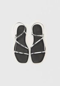 Sorte sandaler med flat såle, med flere sølvfargede metallstropper og ankelspenne. Glatt tekstur, firkantet tådesign.