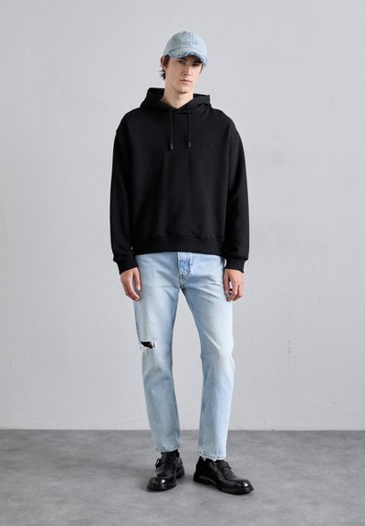 Black hooded sweatshirt with drawstrings, light blue distressed jeans, and black shoes, paired with a light blue denim cap.