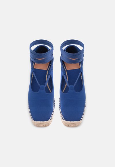 Μοβ καμβά εσπαντρίγιες με λουριά που τυλίγονται γύρω από τον αστράγαλο και φυσικές σόλες από υφαντό τζούτ, εμφανίζονται από πάνω σε λευκό φόντο.