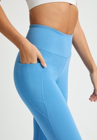 Leggings blu a vita alta con una texture liscia, dotati di una tasca laterale e cuciture piatte, progettati per comfort e flessibilità.