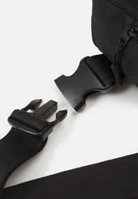Cinghia in nylon nera con una fibbia in plastica, presenta una superficie liscia e lunghezza regolabile. Include dettagli in tessuto e un meccanismo di clip sicuro.
