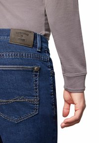 Dunkelblaue Jeans aus Denim mit detaillierten Nähten, einem strukturierten Lederpatch am Bund und einer Seitentasche mit Knopf. Schlanke Passform.