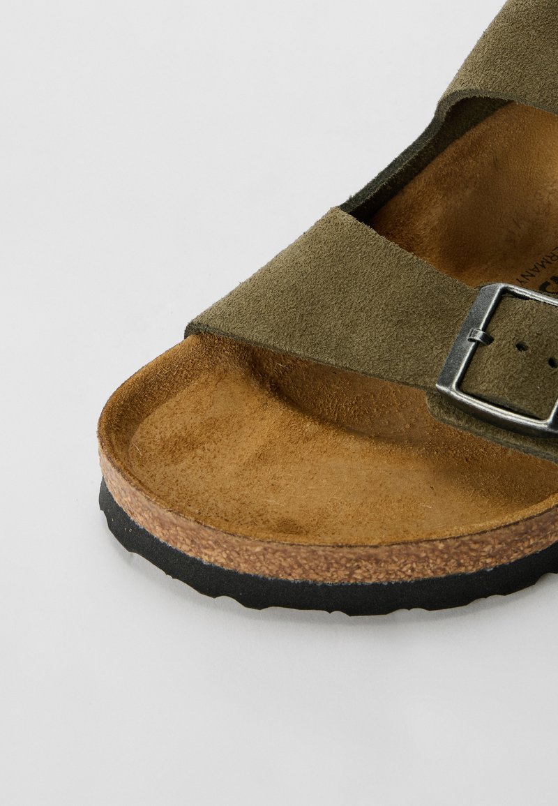 Sandale en suède verte avec deux larges brides, une boucle métallique et une semelle en liège avec une finition texturée beige. Semelle en caoutchouc noir.