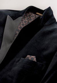 Svart sammetsblazer med mönstrat brunt och svart sidenfoder och matchande näsduk i bröstfickan.
