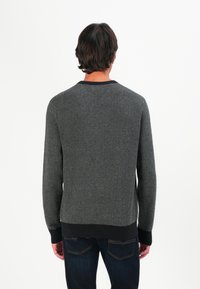 Grauer Pullover mit einem strukturierten Fischgrätmuster, rundem Ausschnitt und schwarzen gerippten Bündchen. Kombiniert mit dunkelblauen Jeans.