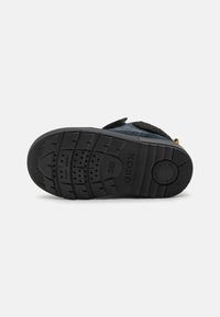 Černá gumová podrážka boty s texturovaným úchopem. Obsahuje kruhové vzory a perforace pro prodyšnost. Lepicí pásek pro uzavření.