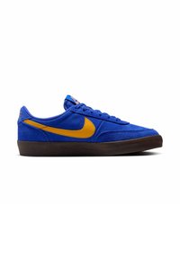 Baskets basses en daim bleu avec un swoosh Nike jaune vif et une semelle marron foncé, vues de l'extérieur.