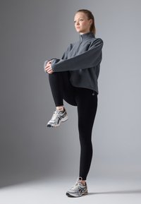 Pullover grigio in pile con mezza zip, abbinato a leggings neri e scarpe da ginnastica bianche con accenti in argento e oro.