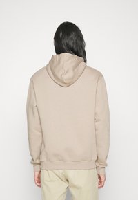 Felpa beige con cappuccio regolabile, polsini e orlo a coste, materiale in misto cotone, caratterizzata da una superficie liscia e un design minimalista.