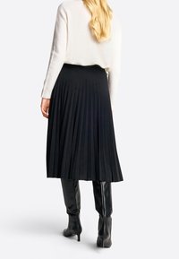 Falda midi plizada negra con una textura suave, combinada con botas de cuero negro hasta la rodilla y un suéter de punto blanco.