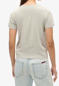 Grå bomulds T-shirt med korte ærmer og rund hals. Bagsiden har en glat tekstur, kombineret med lyseblå denim jeans.