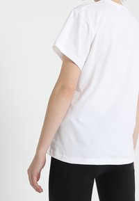 Bílá bavlněná tričko s krátkými rukávy, volný střih a rovný spodní lem. Minimalistický design, žádné vzory ani ozdoby viditelné.