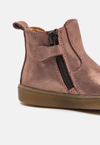 Bota metálica rosa até ao tornozelo com fecho lateral, textura em camurça, bico arredondado e sola de borracha com um padrão texturizado.