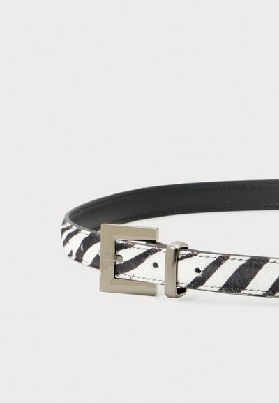Ceinture imprimé zèbre noir et blanc avec boucle rectangulaire argentée et boucle sur un fond clair.