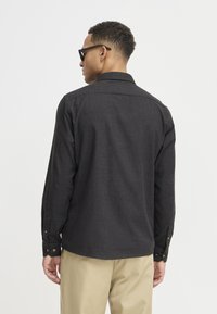 Black long-sleeve button-up shirt with a textured fabric, featuring a collar, button cuffs, and a curved hem, worn with khaki pants.