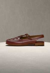 Καφέ δερμάτινο επίπεδο παπούτσι slingback με υφαντή λεπτομέρεια στο μπροστινό μέρος και λουράκι με αγκράφα στο πλάι, πάνω σε ανοιχτή επιφάνεια με γκρι φόντο.