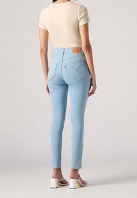 Vaqueros de tiro alto en azul claro con silueta ajustada, que presentan un parche de cuero en la parte trasera y detalles sutiles de costura.