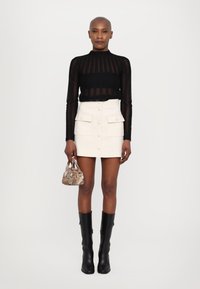 Zwarte doorschijnende top met lange mouwen, witte nauwsluitende mini-jurk met knopen aan de voorkant en zakken, zwarte laarzen tot de knie en een handtas met een patroon.