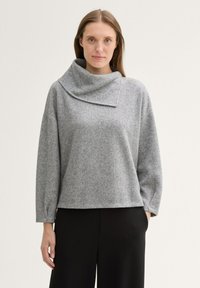Grauer, strukturierter Pullover mit einem Loop-Kragen und weiten Ärmeln, kombiniert mit schwarzen Hosen. Schlichtes Design, mittellang und aus weichem Stoff.