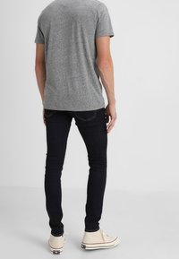 Šedé tričko s krátkým rukávem, tmavé skinny džíny a bílé tenisky s červenými akcenty. Hladká tkanina a přiléhavý střih.