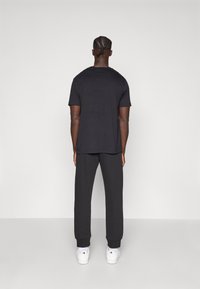 Μαύρο κοντομάνικο μπλουζάκι και σκούρο γκρι φόρμες, και τα δύο από μαλακό ύφασμα. Άσπρα αθλητικά παπούτσια ολοκληρώνουν την αθλητική εμφάνιση.