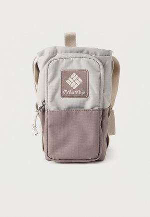 Μικρό τσαντάκι ώμου Columbia σε μπεζ και μοβ, με μπροστινή τσέπη με φερμουάρ και ρυθμιζόμενο λουρί, σε στούντιο φόντο.