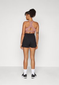 Top de treino rosa com design costas abertas, combinado com calções pretos. O conjunto apresenta um tecido texturizado e é completado com sapatilhas pretas.