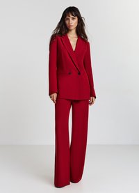 Completo su misura rosso con giacca doppiopetto e pantaloni a gamba larga. Tessuto liscio, revers affilati e due bottoni neri sulla giacca.