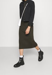 Giacca di jeans nera, gonna midi a coste oliva, borsa bianca e stivaletti neri con suola spessa. Design e materiali semplici ed eleganti.