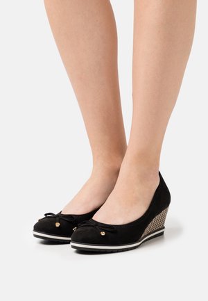 Schwarze Wildleder-Wedge-Schuhe mit runder Zehenpartie, betont durch eine Schleife und goldene Details. Strukturierter Wedge mit einem karierten Muster und weißer Sohle.