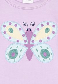 Violetti puuvillapaitako, jossa on perhoskuvio sinisillä siipillä, vihreillä yksityiskohdilla ja violetilla pisteillä. Perhosessa on brodeerattuja yksityiskohtia.