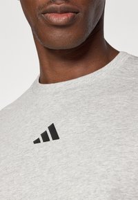 Sweatshirt gris en mélange de coton, avec un logo noir à trois bandes sur la poitrine gauche et un col rond.